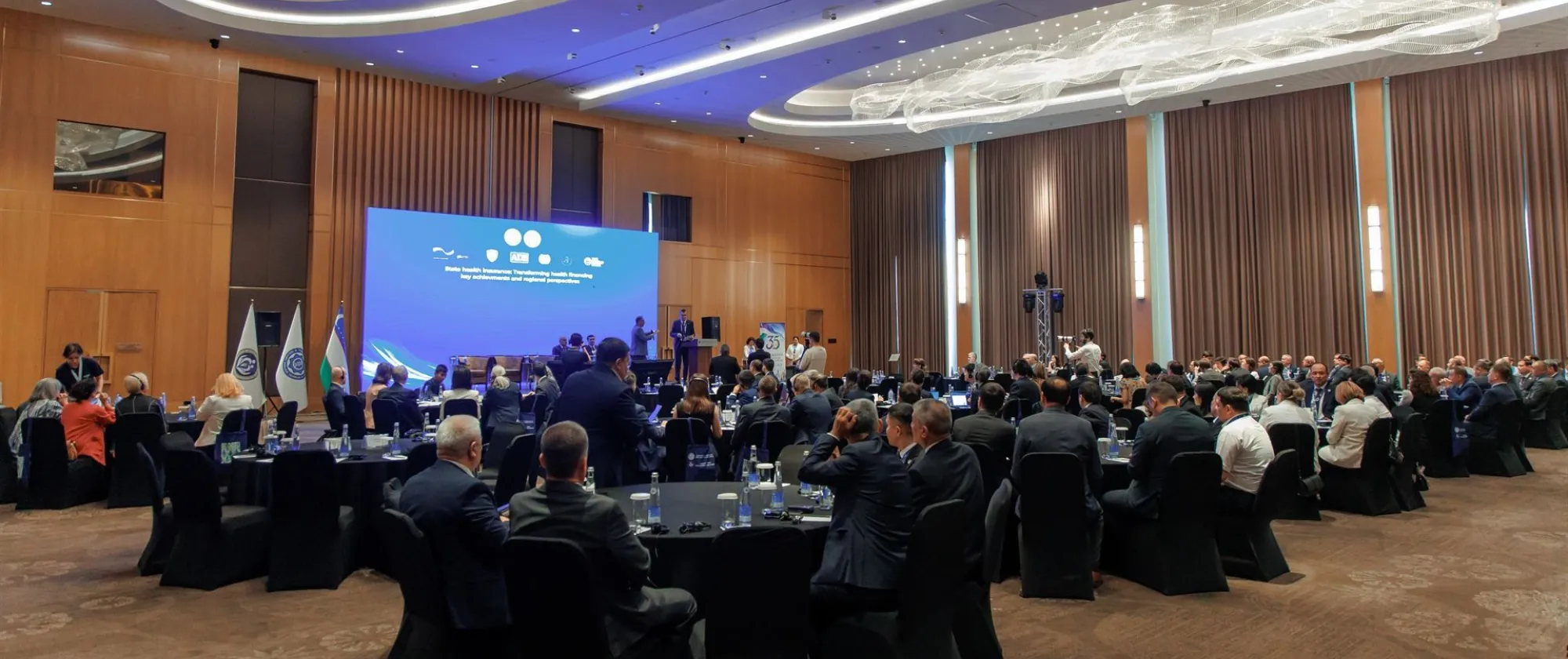 Attendees seated at round tables facing a presentation screen