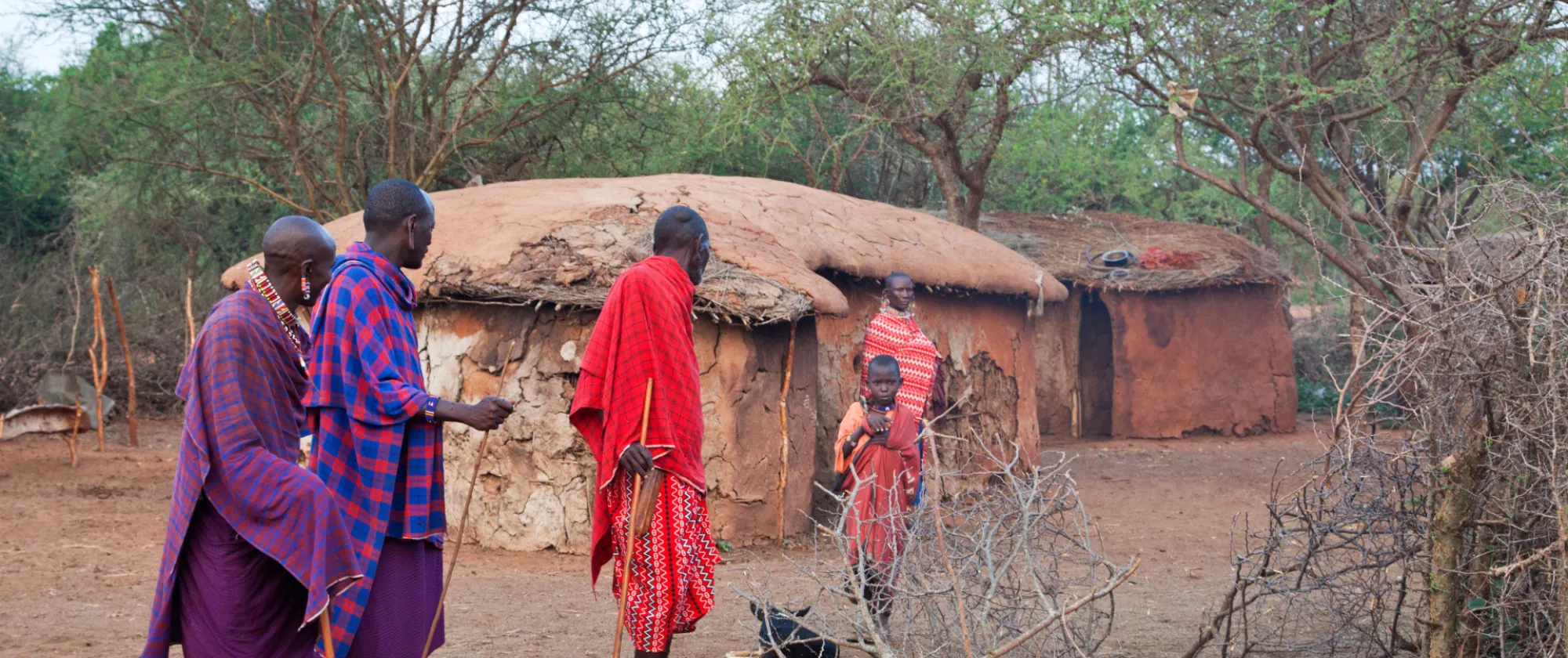 Maasai men leave the homestead as they speak with a woman who remains behind with a child, reflecting gendered patterns of mobility and care responsibilities in pastoral communities in Kenya