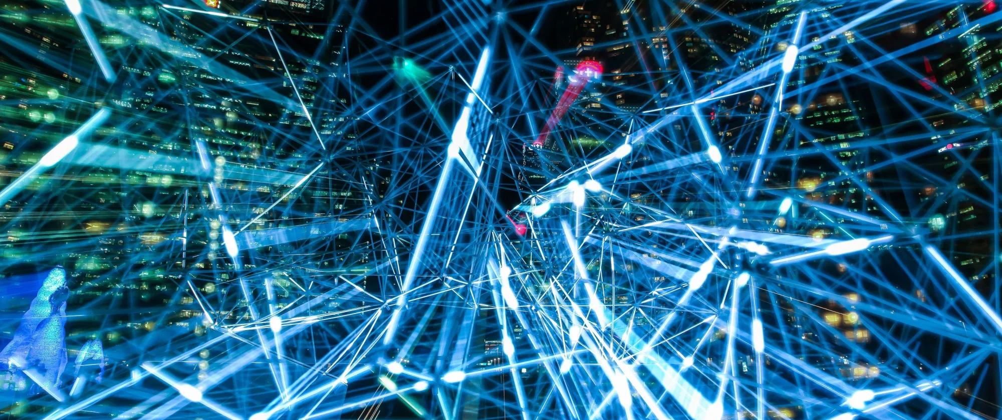 Intersecting blue and white light lines over illuminated city buildings at night.