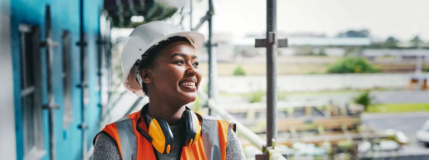 A happy, smiling and cheerful young woman or senior construction industry worker standing at a building site