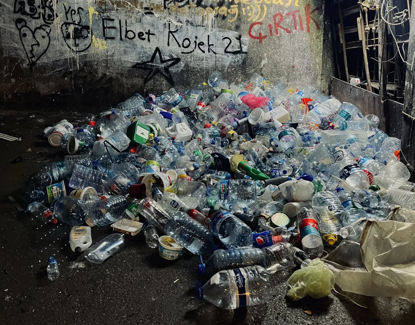 Pile of plastic waste in front of a wall with graffiti, in Turkiye