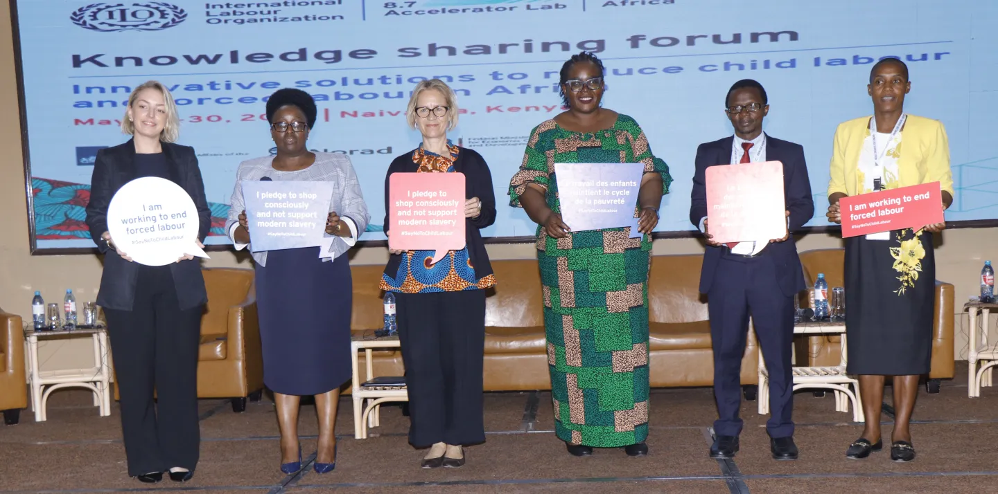 High level panellists pose for a group picture with banners highlighting commitments against child labour