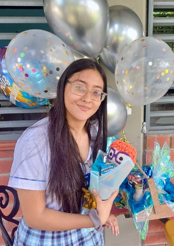 Foto de la joven Valerie Melissa Gómez Rodríguez tiene cabello láceo y largo, castaño con lentes, está uniformada, alrededor de ella unas bombas