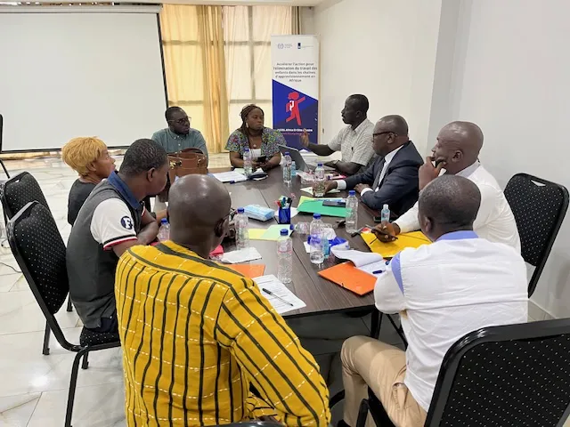 Participants discuss in a group work, in the back there is a banner with the icon of a kid going to school