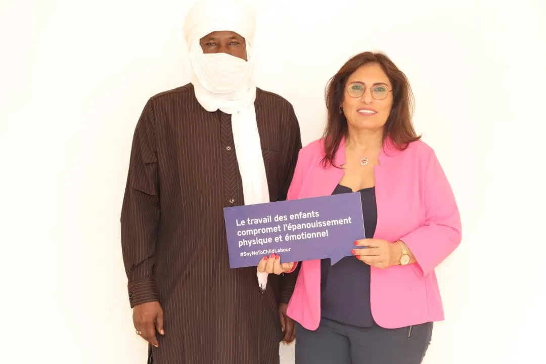 A participant poses together with an ILO staff with a banner that states a quote against child labour