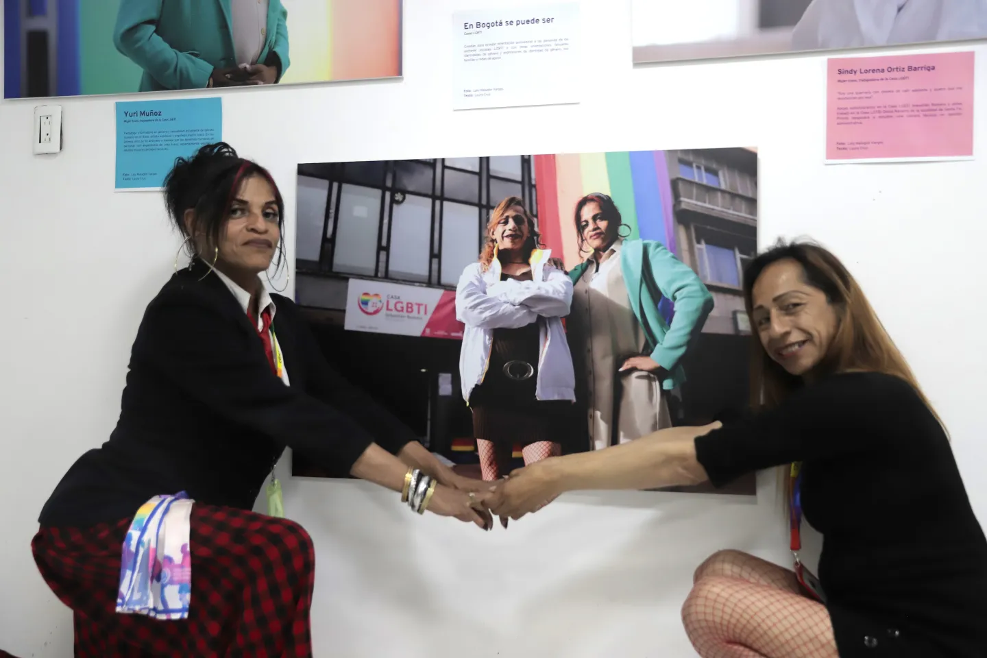 Foto en la que aparecen dos mujeres trans agarradas de la mano junto a una fotografía de la exposición en las que ellas están retratadas