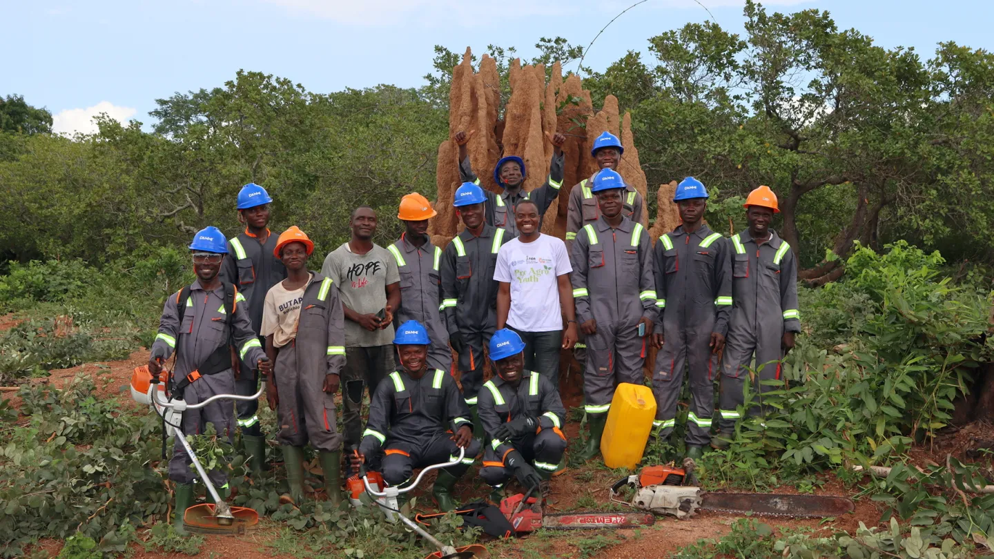 A group of young men, project beneficiaries of the ILO ProAgro YOUTH project, pose together in front of a large termite mound in an orchard near Ferkessédougou, Côte d'Ivoire, on 19 September 2024.
