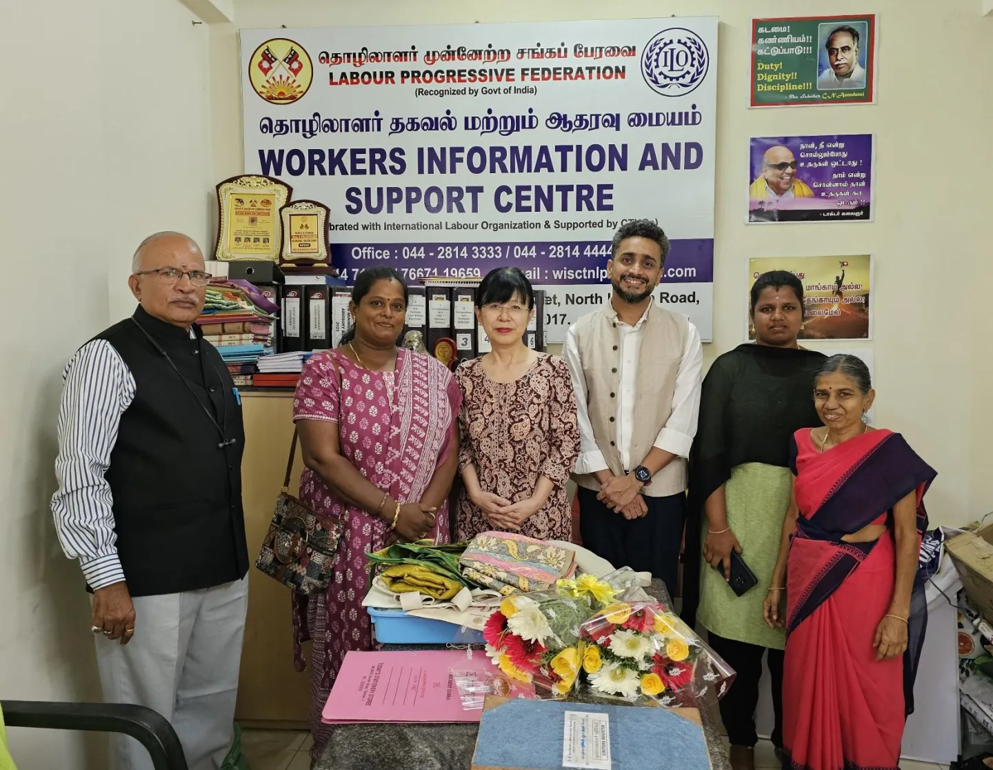 Four women and two men standing together in a small office