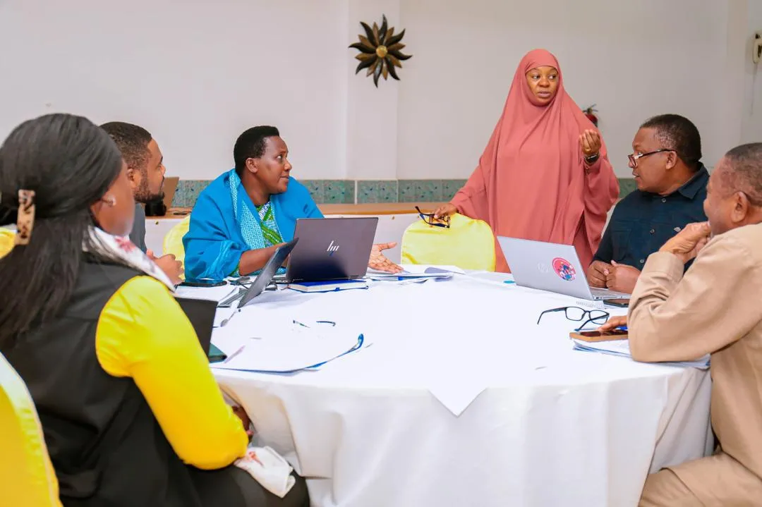Group discussion with a lady standing and speaking to a group sitting around a table. 