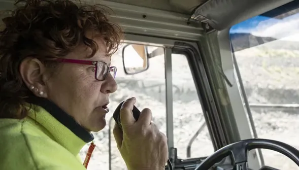 A woman wearing glasses speaks on a radio device inside a truck