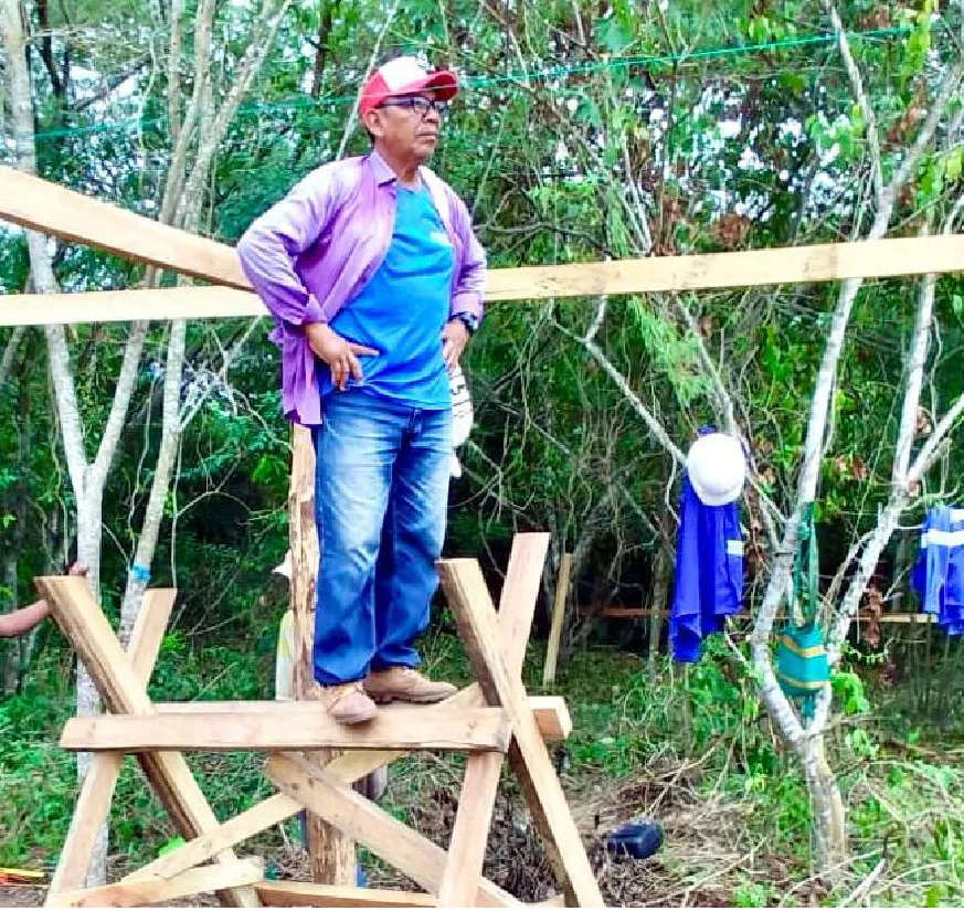 Foto de Nestor sobre una estructura hecha de madera luciendo ropa de trabajo