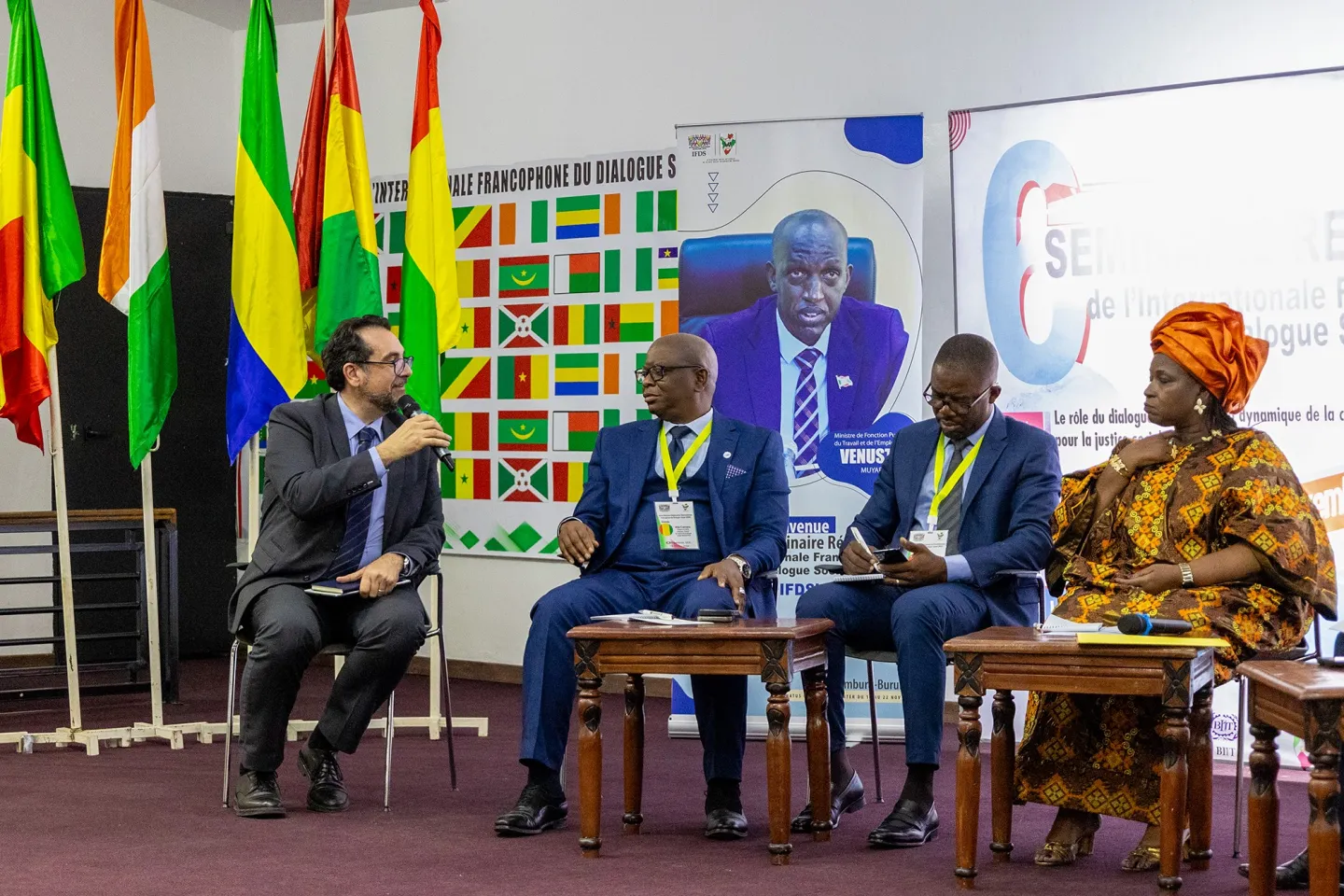 Plusieurs participants au symposium sont assis sur la scène, prenant part à un panel de discussion sur les défis et les opportunités du dialogue social dans leurs pays respectifs.