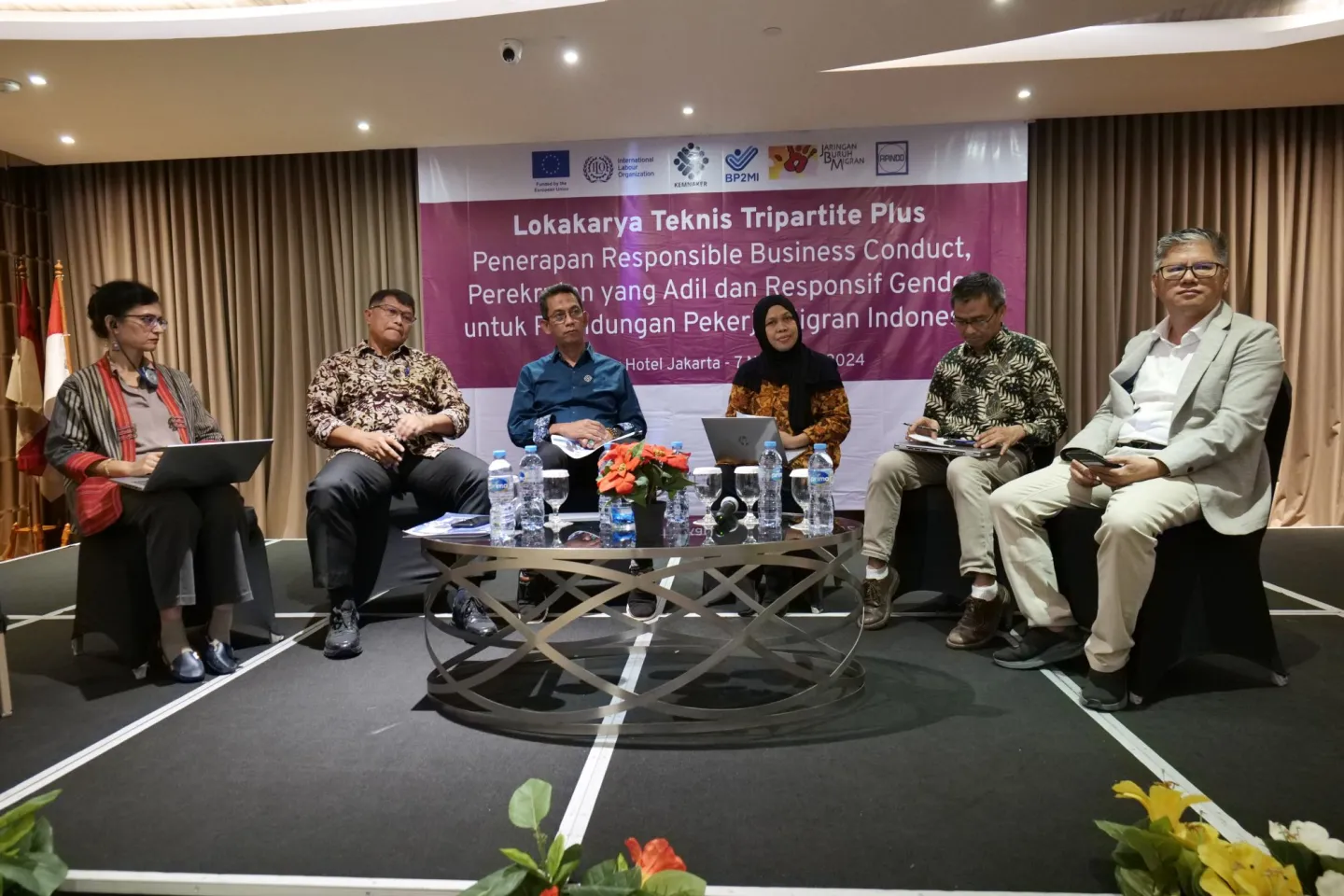 Three women and three men sittting on the stage with an event backdrop at the back.