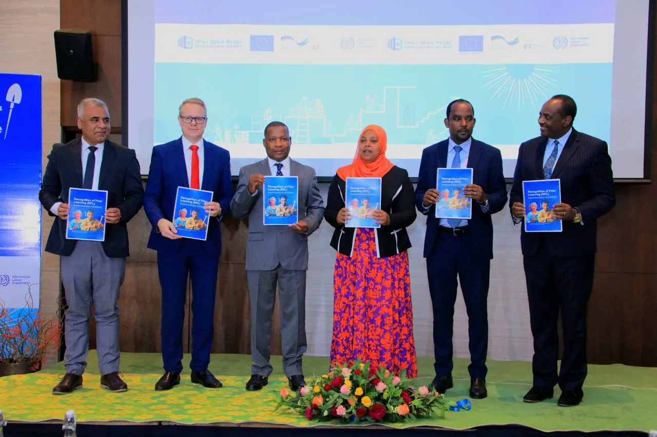 Five men and one woman standing with a publication on their hand. 