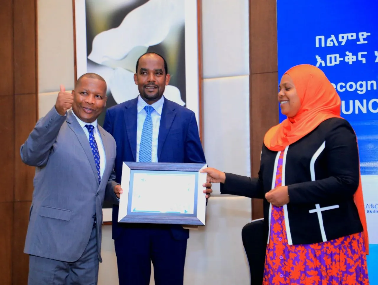 A aman receiving a framed certificate from a woman and showinh thumbs up. 