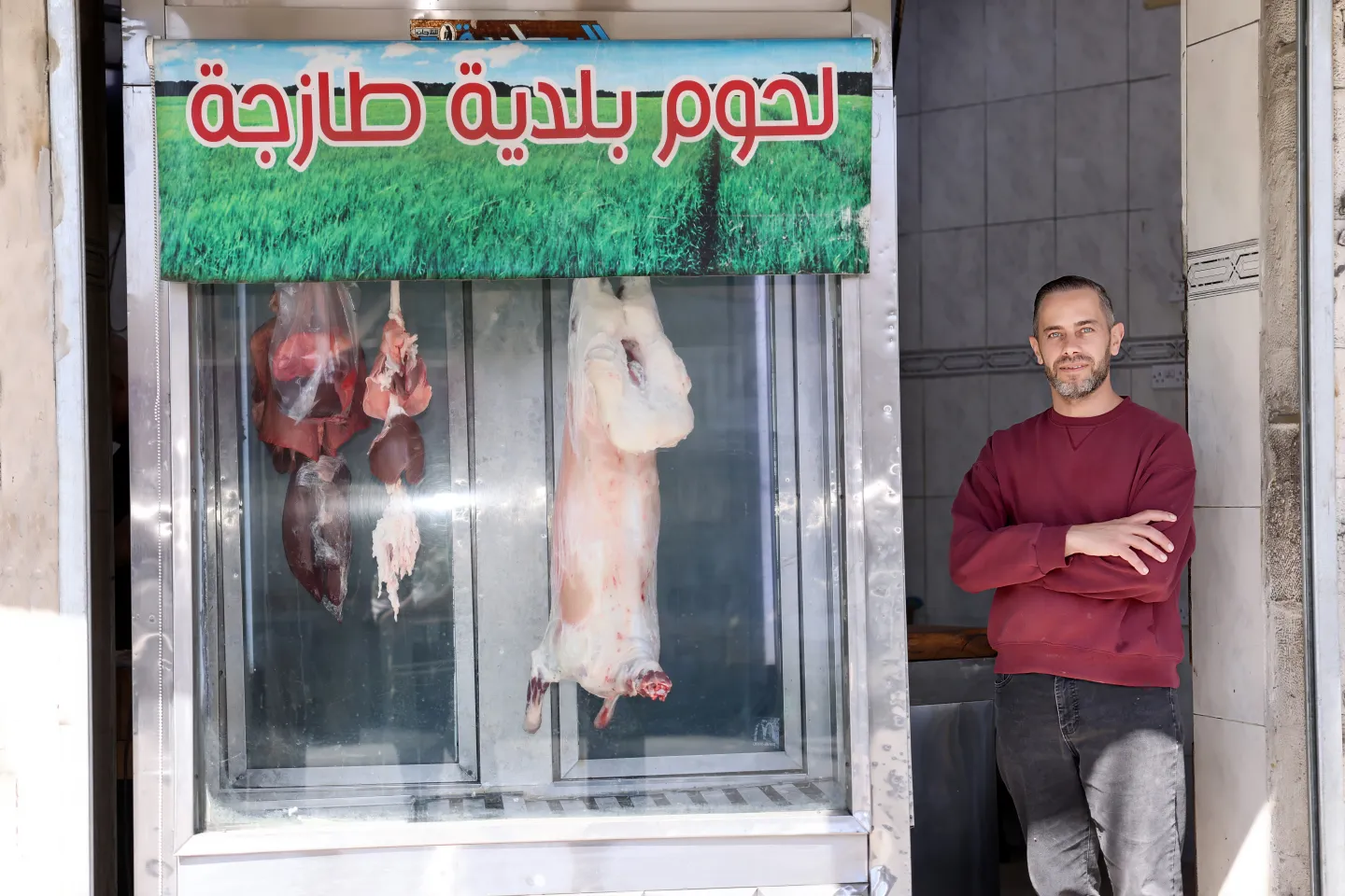 Eyad stands at the entrance of the butcher shop where he works.