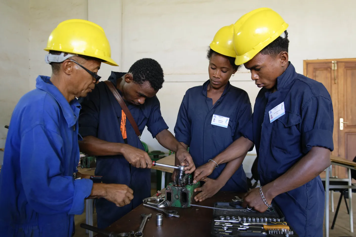 3 people wearing yellow helmets are learning new skills in mechanics