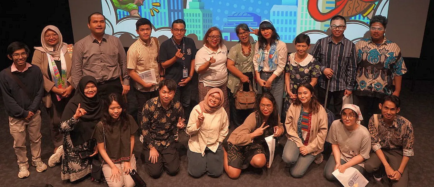 A group photo of participants and panelists in front of the stage.