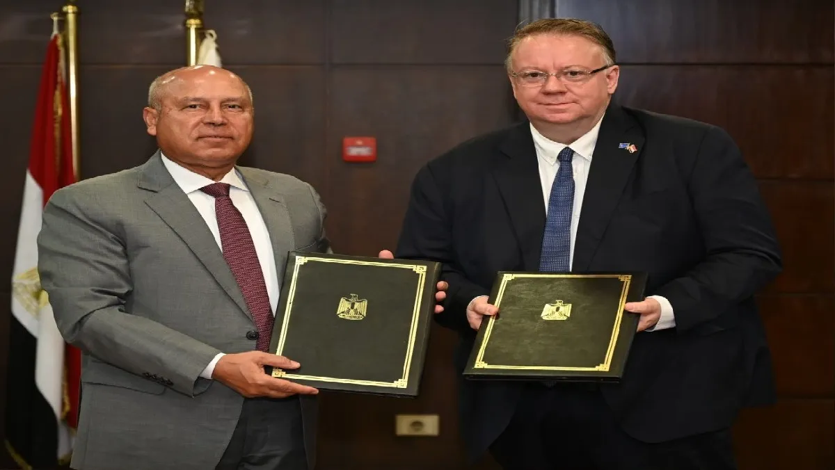 Two officials holding signed documents during a formal ceremony in front of the Egyptian flag, highlighting international collaboration and diplomatic agreements.