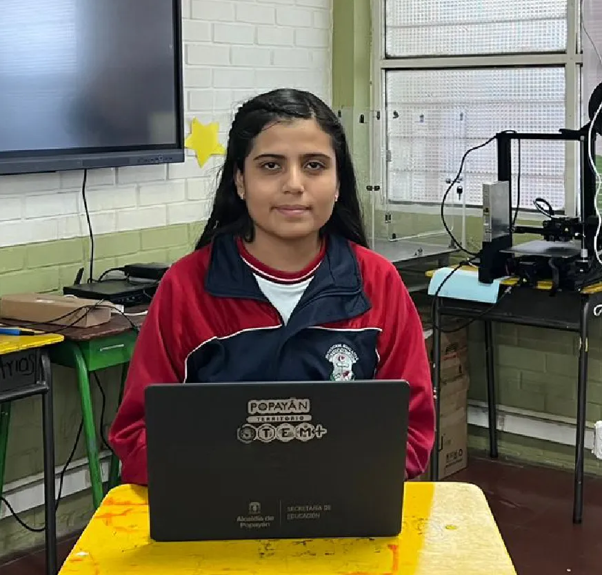 Mujer en aula de clases desarrolla labores informáticas con un portatil.