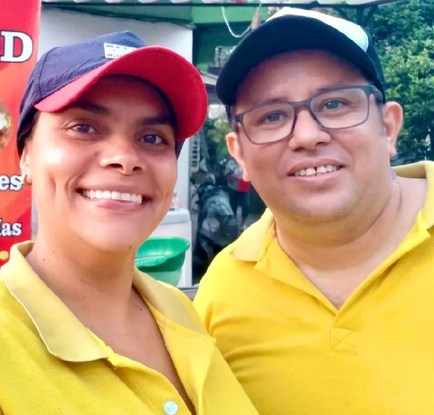 Mujer junto a hombre sonríen con orgullo, atrás aviso de venta de comidas rápidas. 