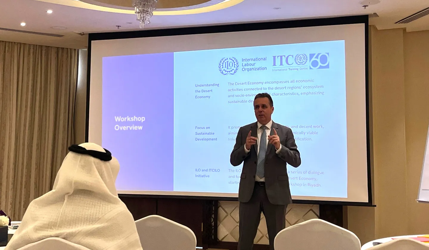 ILO Deputy Regional Director for Arab States for ROAs standing in front of a projector screen and giving a speech