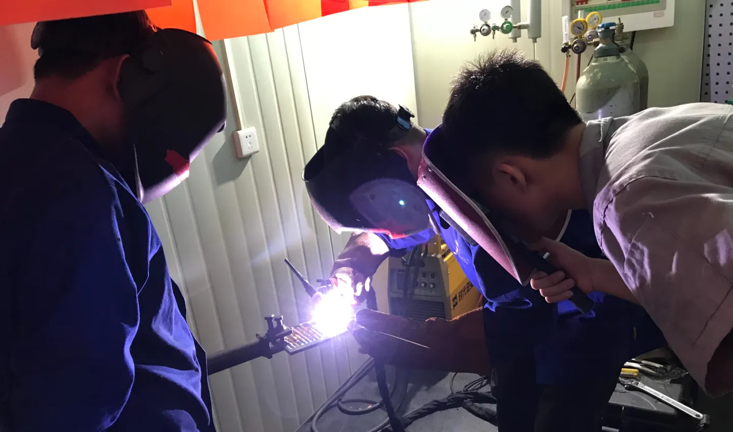 Three men wearing protective face gears are welding. 