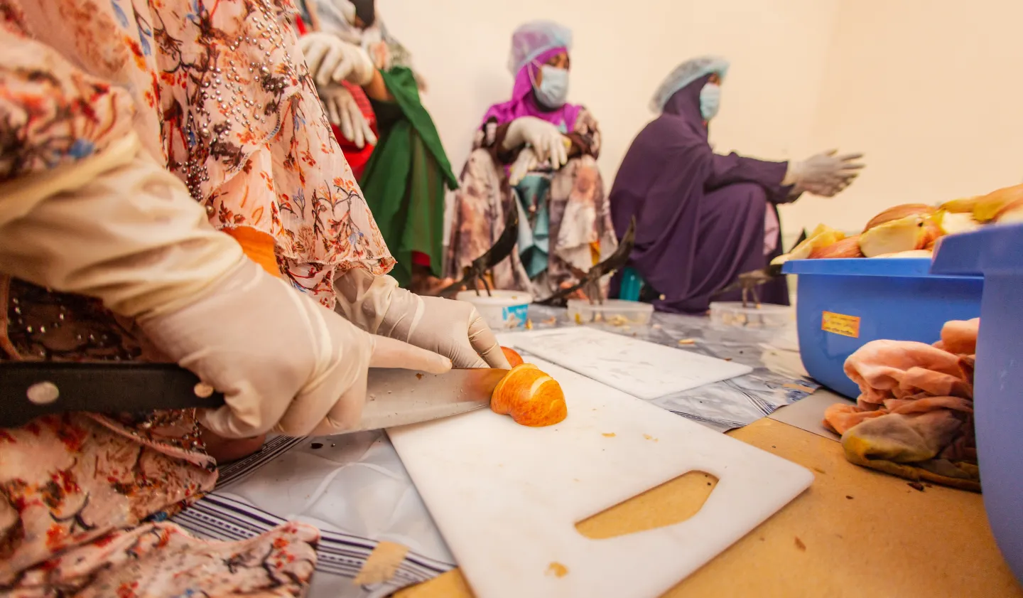 A lady wearing white gloves is chopping ingredients.
