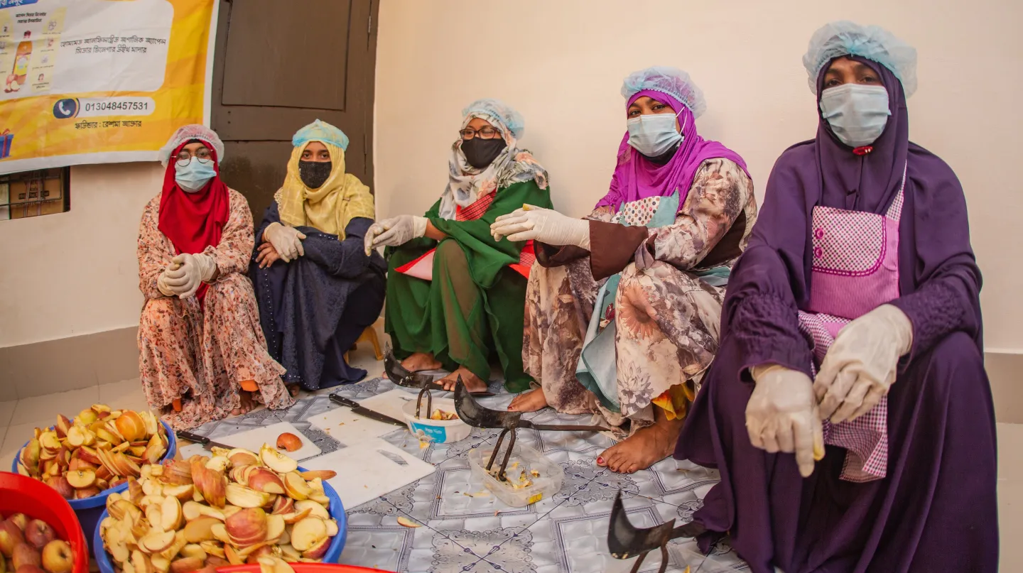 Female workers sit next to trays of fruits. 