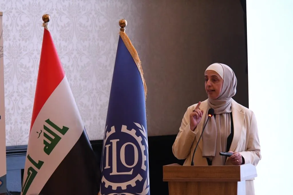 a woman giving a speech with ILO and Iraqi fag in the background