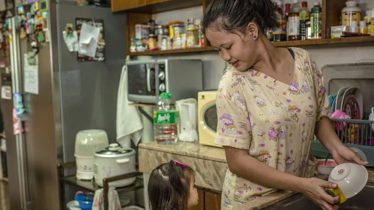A domestic worker cleaning dishes and looking after a child.