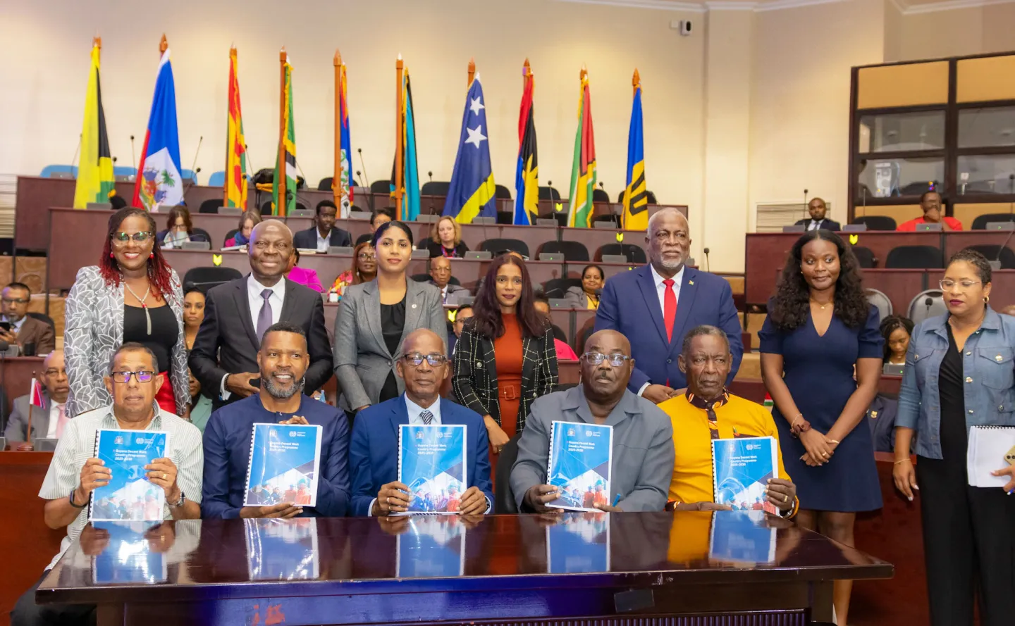 Signatories pictured holding copies of the signed Decent Work Country Programme (DWCP) for Guyana. National flags of Caribbean nations are displayed in the background.