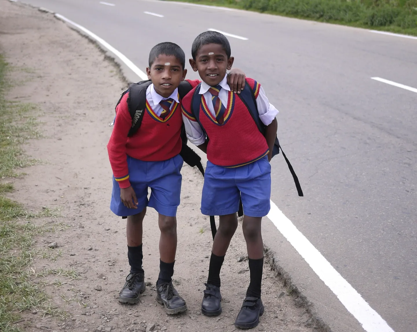 two young boys dressed in school uniforms, and red sweaters, smile at the camera