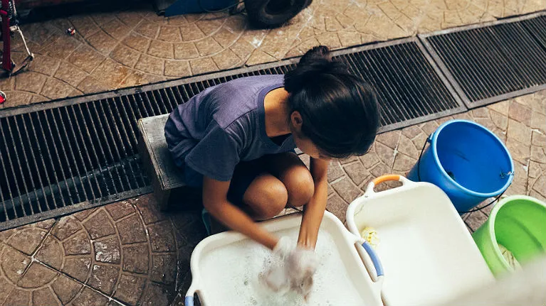 A women migrant domestic worker cleaning dishes.