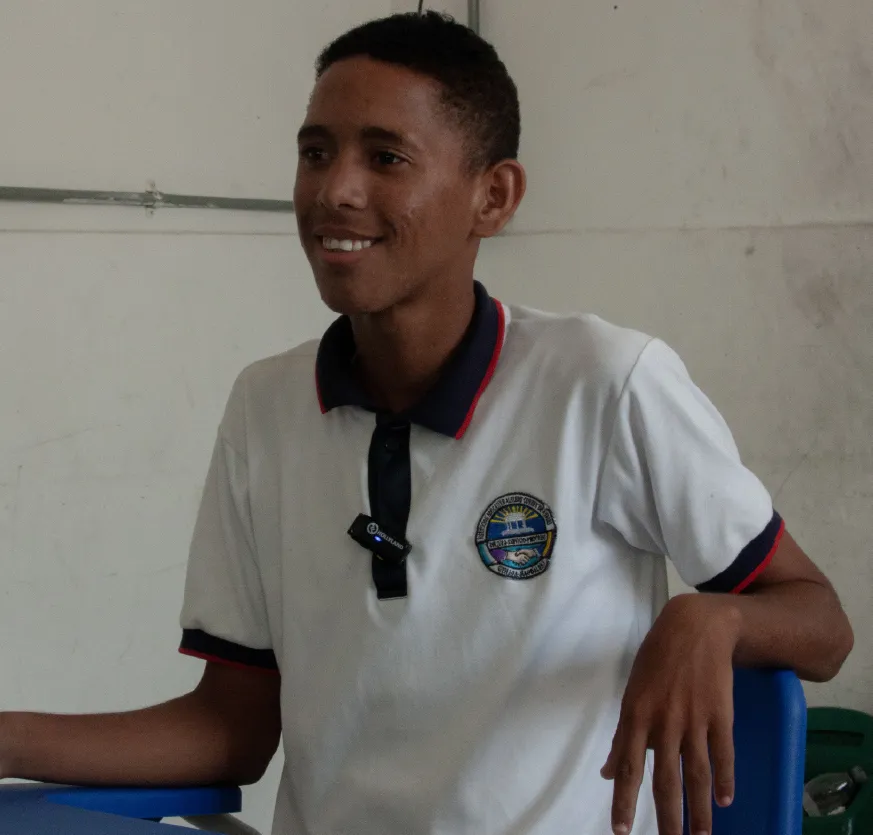 Hombre joven y sonriente con uniforme de estudiante, de fondo un tablero blanco.