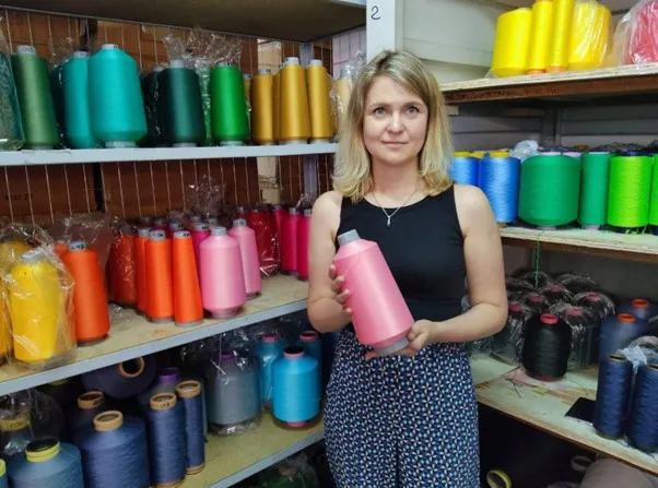 Woman in front of colourful industrial thread rolls