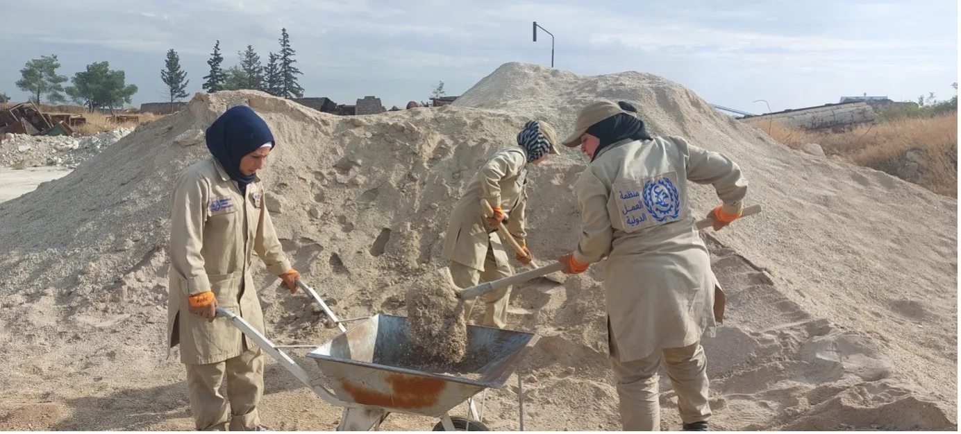 Three women in Aleppo, Syria shoveling recycled gravel into wheelbarels