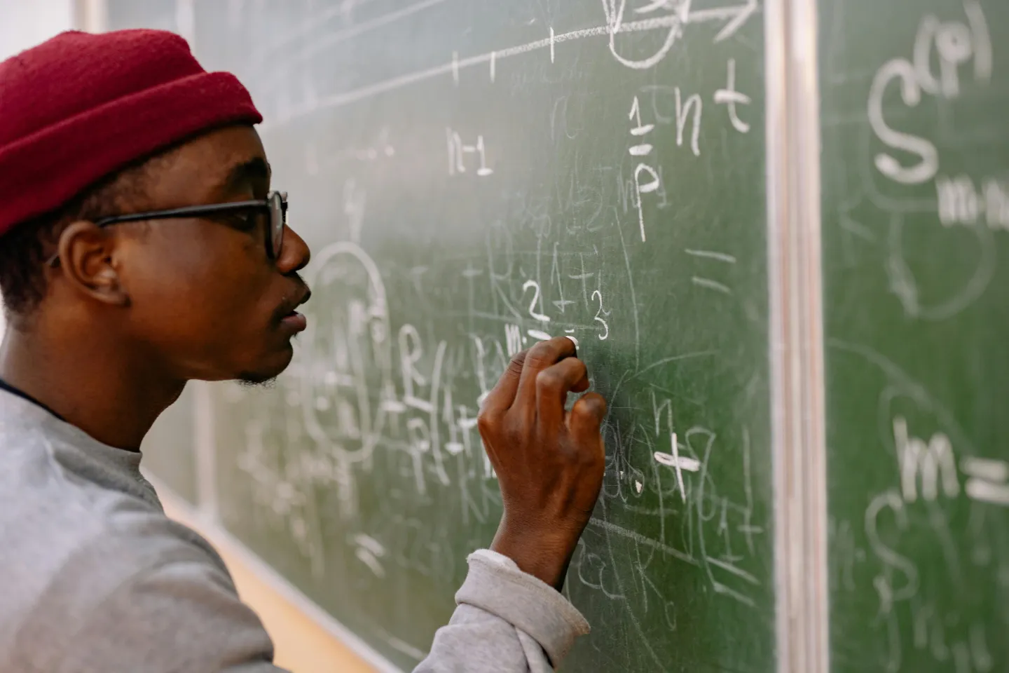 A young man is writing calculations on a black board