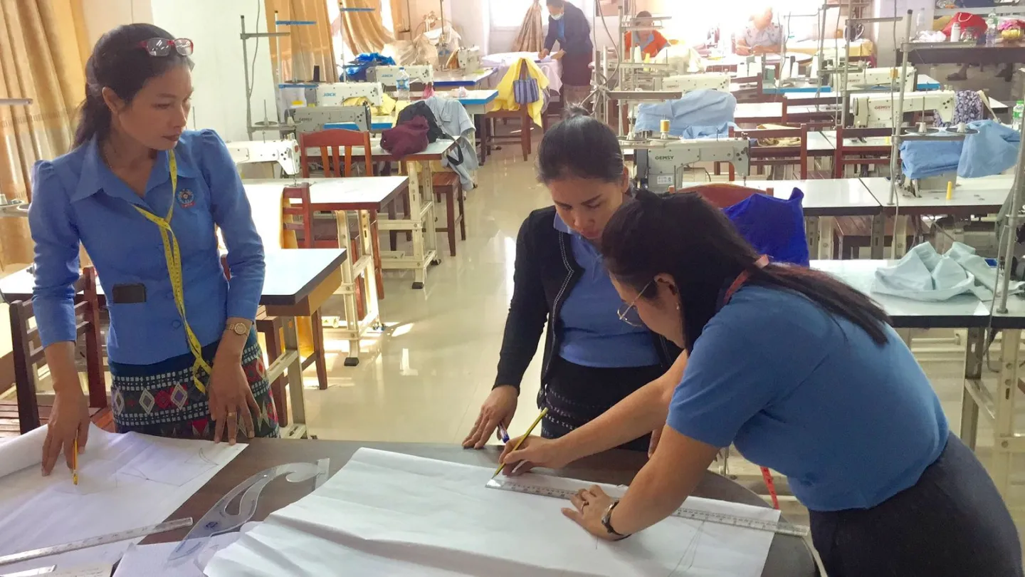 Ladies are measuring sizes on paper clothing cutouts while one observes.
