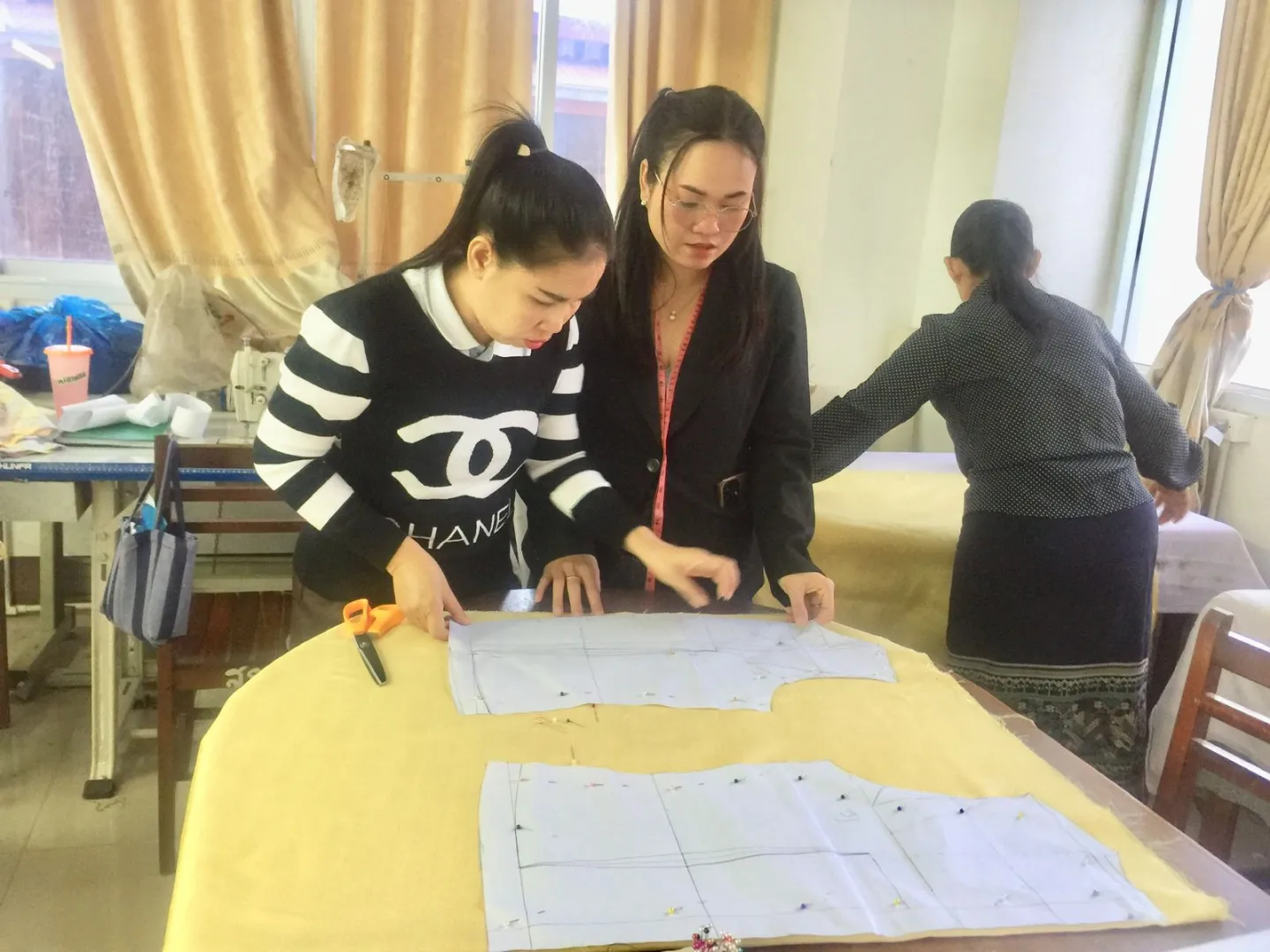 Two ladies are measuring sizes on paper clothing cutouts.