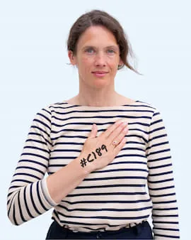 A woman is facing the camera with her hand on her heart and #C189 written on the back of her hand.