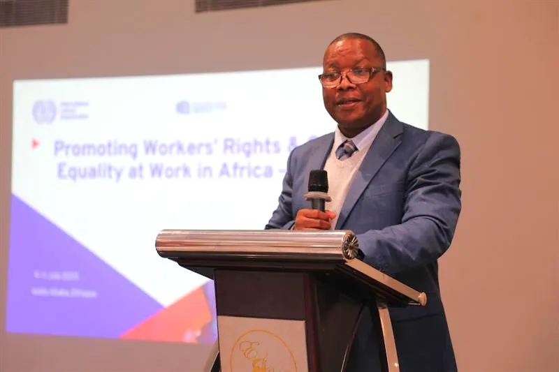 Man in a suit speaking infront of an audience. 