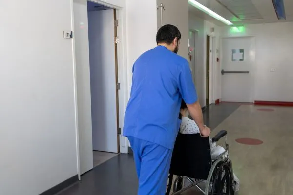 Marwan in his nurse outfit pushing a patient in his wheeled chair