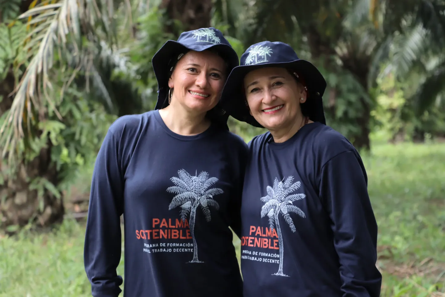 Dos mujeres sonrientes posando en una plantación de palma de aceite.