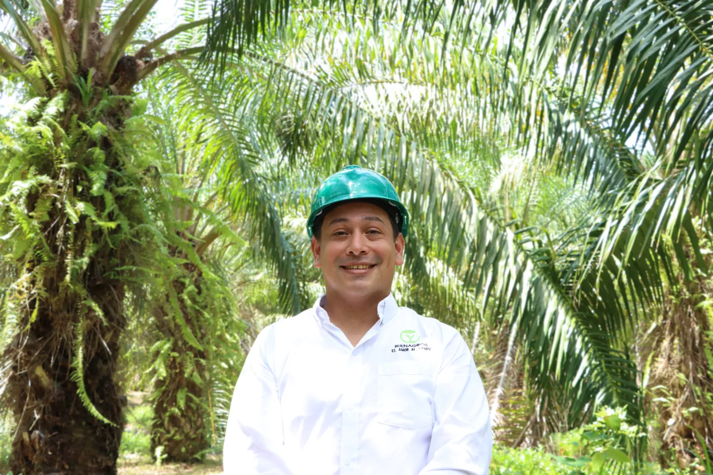 Un hombre posa sonriendo con el fondo de una plantación de palma de aceite. 