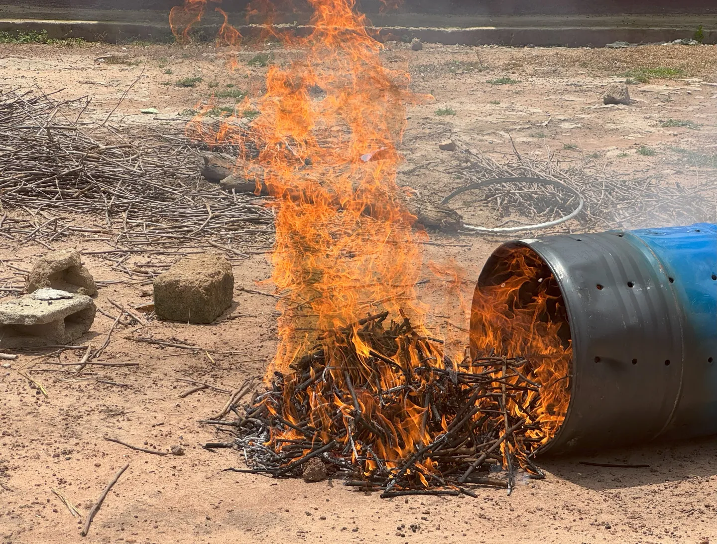 Le carbonisateur renversé, la flamme va s’éteindre sous le sable, révélant le biochar : un trésor pour des sols fertiles et des vies transformées.