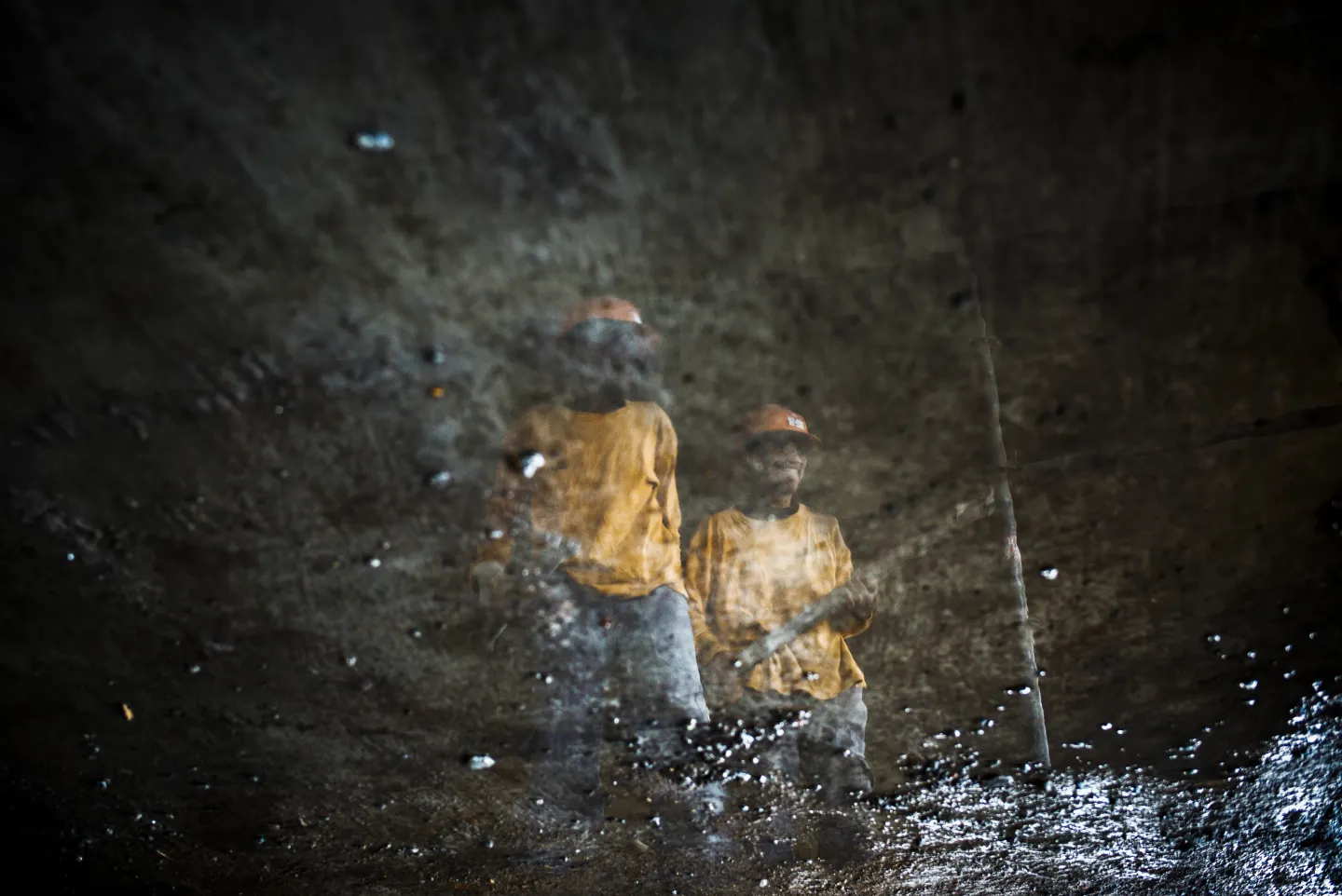 The mirrored reflection of two Malagasy construction workers captured in a puddle of water.