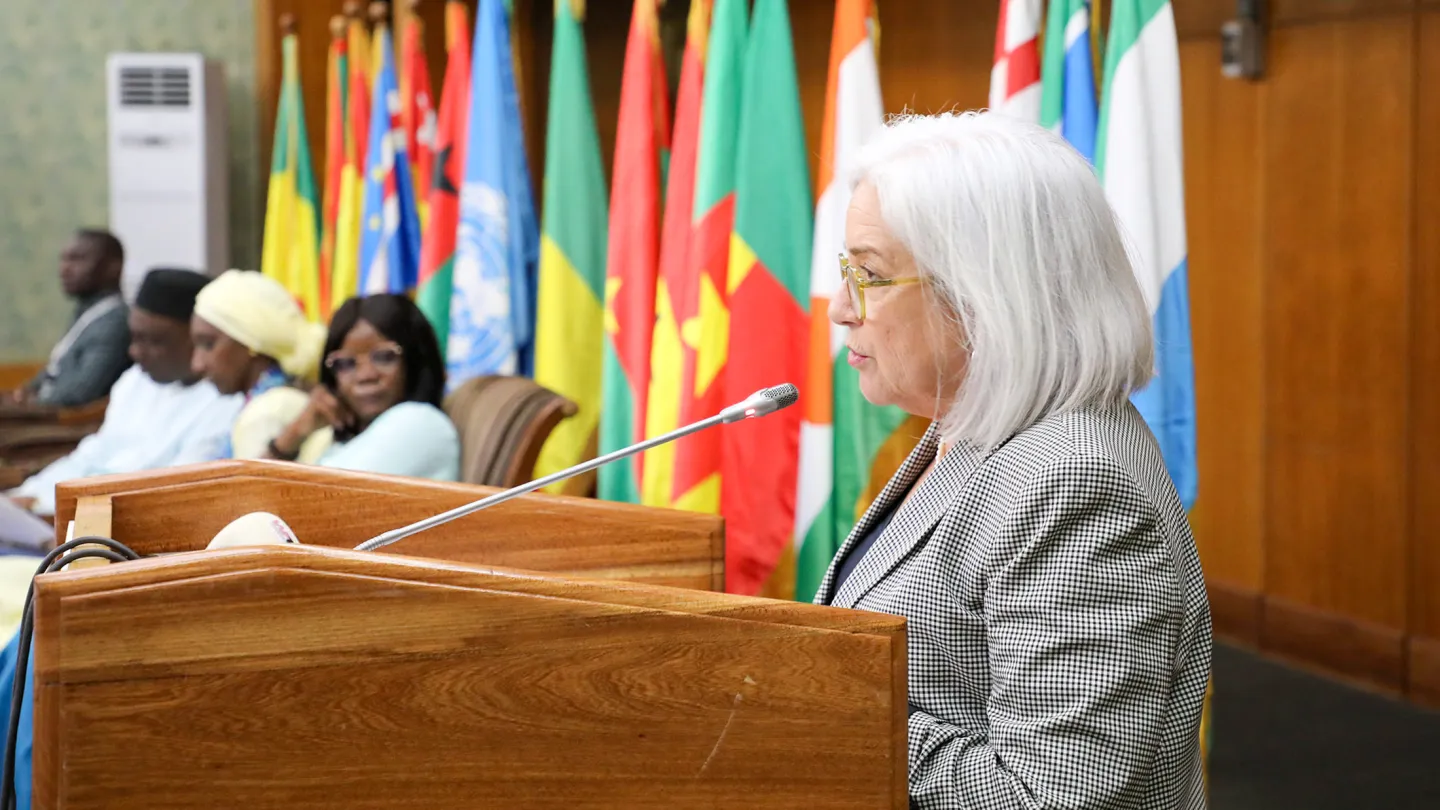 Ms. Barrie Freeman, Deputy Special Representative of the United Nations Secretary-General for West Africa and the Sahel, speaks at the opening of the 4th Annual West Africa and Sahel Youth Forum in Dakar, standing at a podium with microphones, with country flags displayed in the background.
