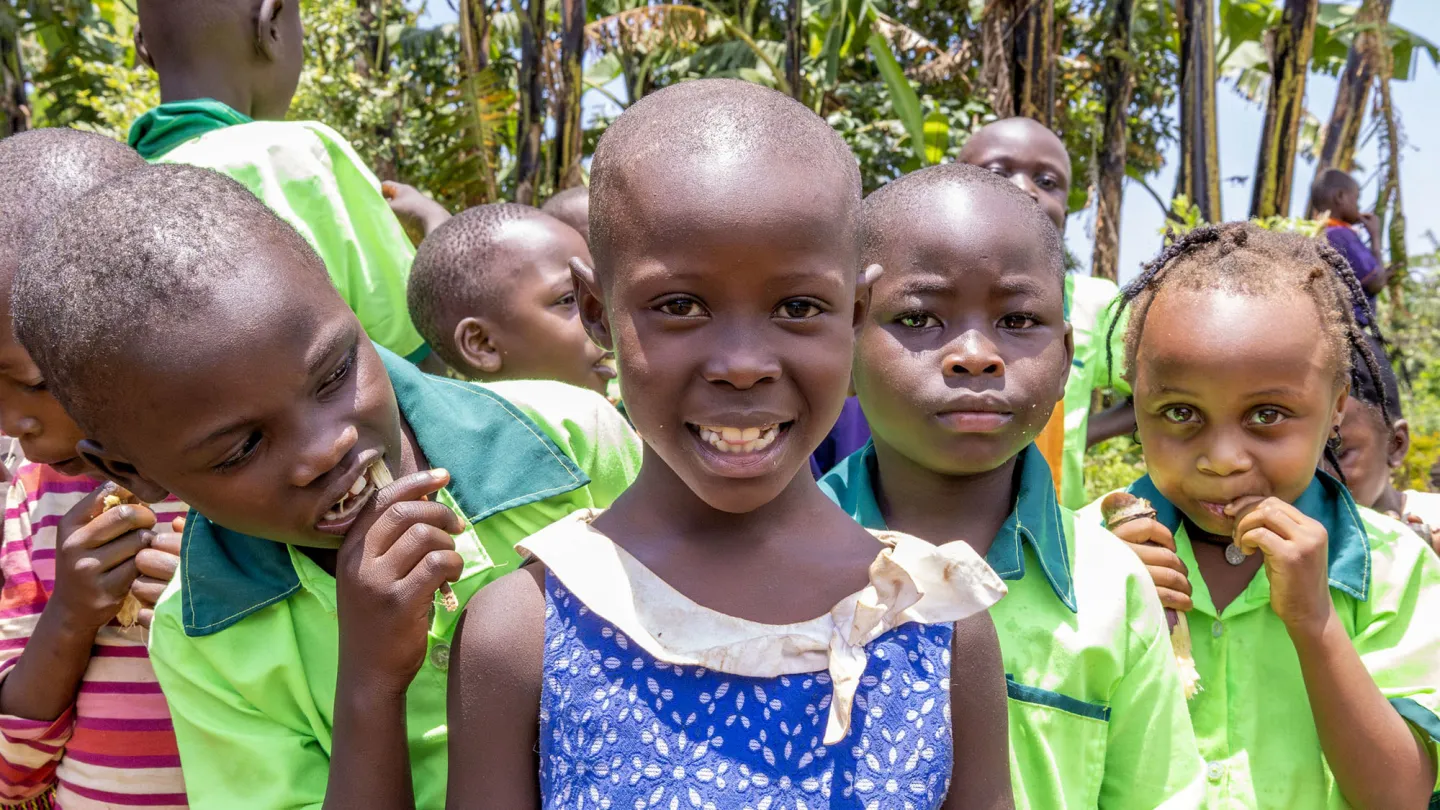 A group of young children smile and play together outside their community kindergarten in rural eastern Uganda.
