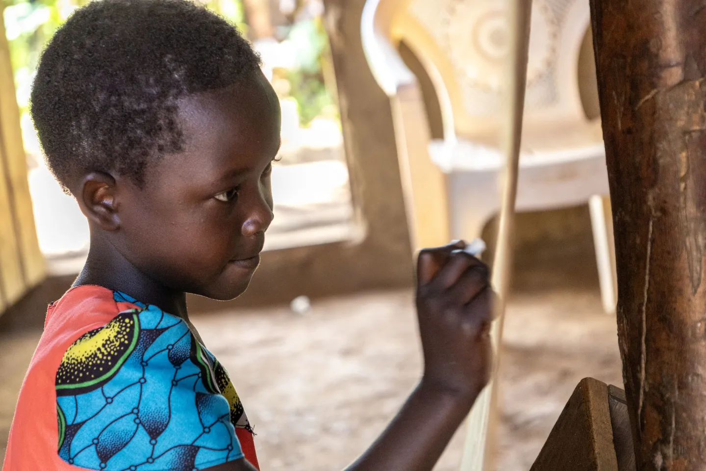 A young girl focuses as she writes on a chalkboard during class in a community school in rural eastern Uganda.